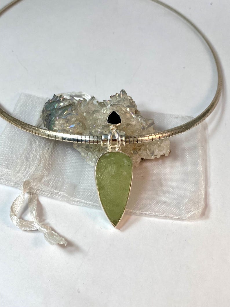 May include: A silver chain necklace with a teardrop-shaped pendant featuring a green stone and a black triangular stone at the top.