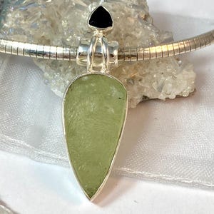 May include: A silver pendant necklace with a light green teardrop-shaped stone and a black triangular stone at the top.