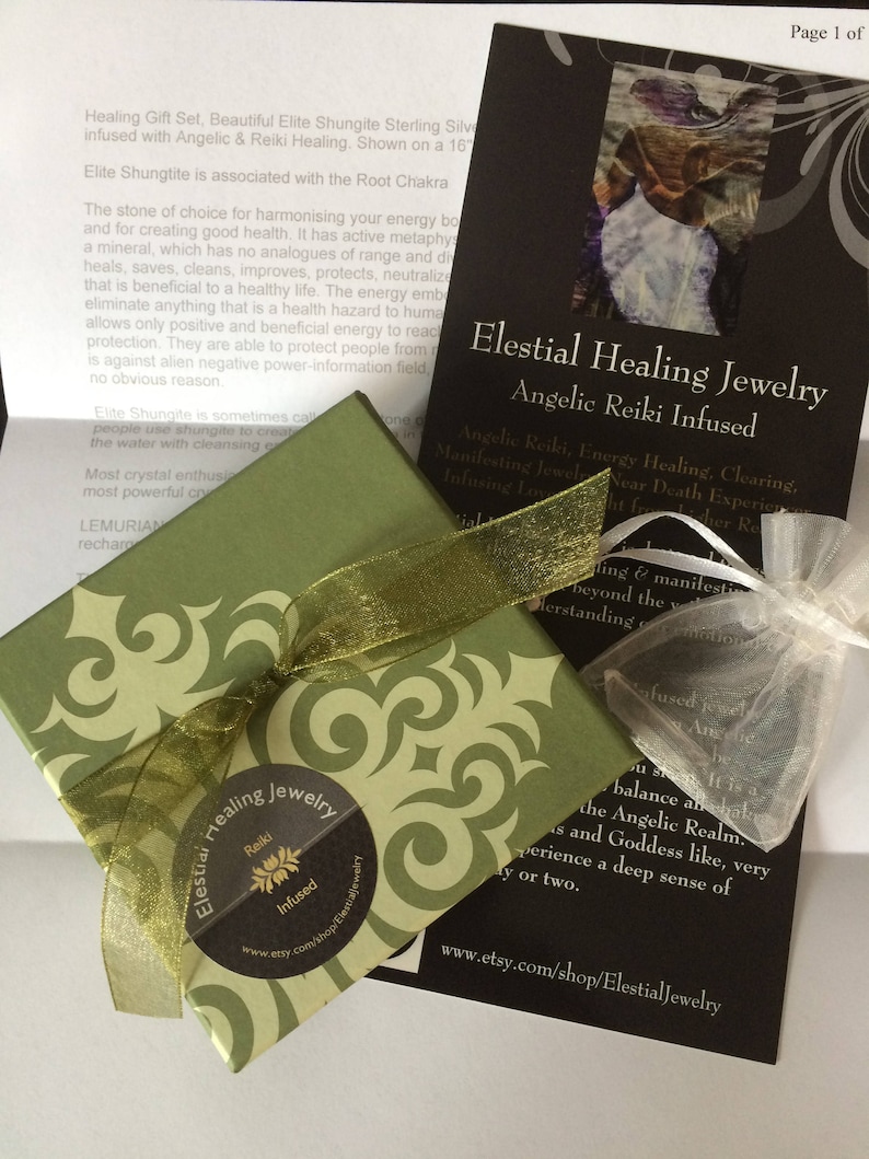 May include: A green gift box with a gold ribbon and a sticker that says "Elestial Healing Jewelry Reiki Infused". The box is sitting on a white surface next to a black card with the text "Elestial Healing Jewelry Angelic Reiki Infused" and a website address.
