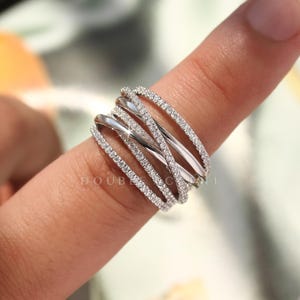 May include: A silver ring with multiple bands, some encrusted with small, sparkling stones. The ring has a modern, interwoven design. The word "DOUBLE EXCELLENT" is partially visible on the ring.