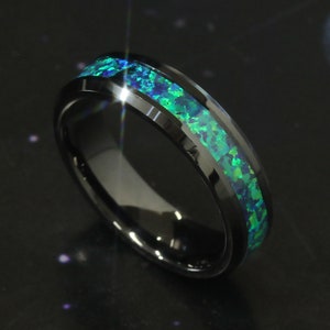 May include: A black tungsten carbide ring with a green opal inlay. The ring has a beveled edge and a polished finish.