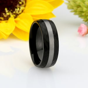 May include: A black tungsten carbide ring with a hammered finish and a silver inlay. The ring is a classic style and is perfect for a wedding band or an everyday ring.