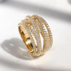 May include: A gold-toned ring with multiple bands, each encrusted with small, sparkling gemstones. The ring has a woven design, and the text "DOUBLE ACCENT" is visible on the side. The ring is set against a white background.