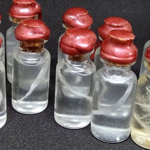 May include: A collection of small glass bottles with red lids and white string-like objects inside. The bottles are arranged in a row on a black surface.
