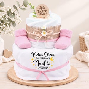 Könnte beinhalten: Eine Windeltorte mit zwei Ebenen aus weißem Stoff, rosa Babyschuhen und einem Holzschild mit der Aufschrift New To The Crew. Auf der unteren Ebene steht der Text Meine Eltern SIND JETZT AUCH Nachts ERREICHBAR mit gelben Sternen und Mond.