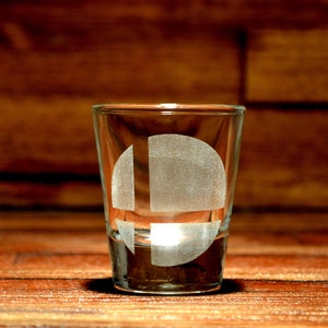 May include: A clear glass shot glass with an etched white Nintendo Smash Bros. logo.