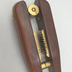 Puede incluir: Un cascanueces de madera con detalles en latón. El cascanueces tiene una mandíbula articulada con un engranaje de latón y una perilla de latón en la parte superior.