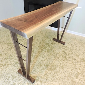 May include: A wooden bar table with a live edge walnut top and a metal frame. The table has a natural wood finish and a modern design.