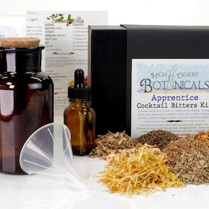 May include: An Apprentice Cocktail Bitters Kit from High Desert Botanicals. The kit includes a dark glass bottle with a cork stopper, a small dropper bottle, a funnel, and various herbs and spices. A black box with a label is also included.