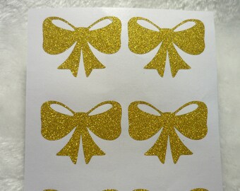 Può includere: Un foglio con sei adesivi a forma di fiocco in glitter dorati. I fiocchi sono tutti della stessa dimensione e forma, e sono disposti in due file da tre.