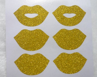 Könnte beinhalten: Sechs goldene Glitzerlippen-Aufkleber auf einem weißen Blatt Papier.