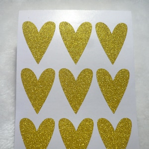 May include: A sheet of nine gold glitter heart stickers. The hearts are arranged in three rows of three.