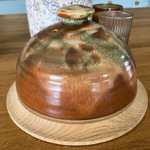 May include: A brown and green glazed ceramic dome with a wooden base. The dome has a mottled glaze with brown, green, and white accents.