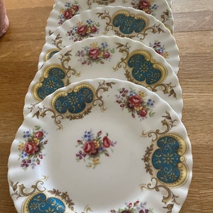 Peut inclure: Ensemble de six assiettes en céramique blanche avec un motif floral et une bordure dorée. Les assiettes ont un bord festonné et un motif bleu et or au centre.