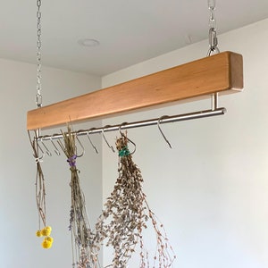May include: A wooden hanging rack with a stainless steel rod and hooks. Dried flowers and plants are hanging from the hooks.
