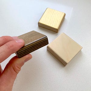 May include: Three wooden squares, one is light brown, one is dark brown with wood grain, and one is a light beige color.