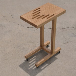 May include: A wooden side table with a rectangular top and a unique design featuring a series of slots cut into the surface. The table has a simple, modern design and is supported by a sturdy, rectangular frame with four wheels.