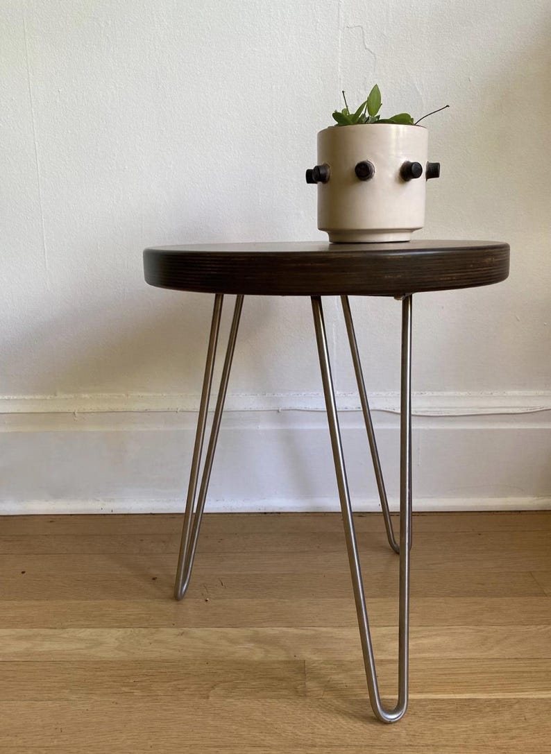 Puede incluir: Una mesa redonda de madera marr&oacute;n oscuro con patas de horquilla. Un macetero de cer&aacute;mica blanca con detalles negros se encuentra encima de la mesa.