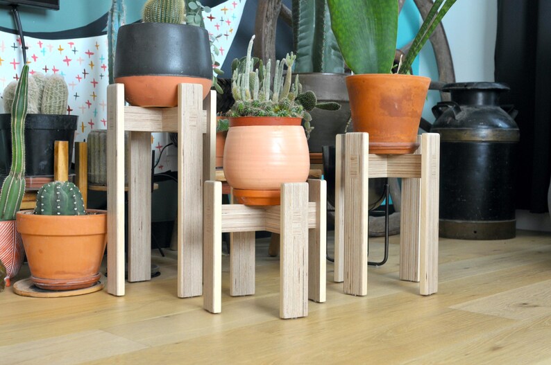 May include: Three wooden plant stands with different sized pots and plants. The stands are made of light wood and have a simple design. The pots are all different colors and styles.