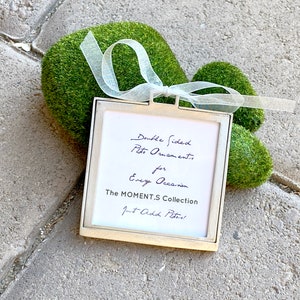 May include: A silver picture frame with a white mat and a handwritten message that reads "Double Sided Photo Ornaments for Every Occasion The MOMENT.S Collection Just Add Photos!"