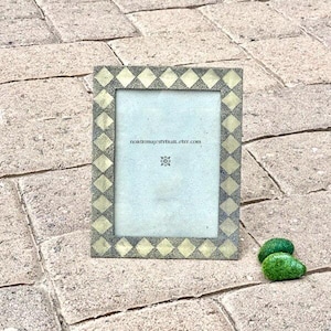 May include: A rectangular picture frame with a diamond pattern in gold and gray. The frame has a white interior and the text "noktilmajestykall.etsy.com" is visible. Two small green decorative stones are in the lower right corner.