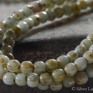 May include: A strand of light green glass beads with brown speckles. The beads are round and have a smooth, glossy finish.