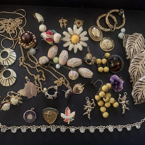 May include: A collection of vintage jewelry, including necklaces, earrings, brooches, and rings. The pieces feature various designs, such as floral, leaf, and geometric shapes, in gold and silver tones. Some items have colorful accents.