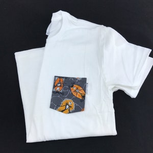 May include: White t-shirt with a pocket featuring a black and white print of Jack Skellington and Sally from The Nightmare Before Christmas. The print is in orange and grey.