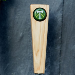 May include: A wooden beer tap handle with a green and yellow circular logo featuring a white stylized letter "T" and a white axe.