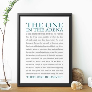 May include: A black framed print with a white background and teal text. The quote reads "The One in the Arena" by Theodore Roosevelt. The quote is about the importance of action and striving for greatness.