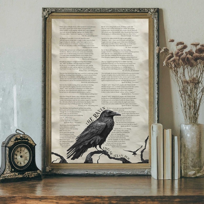 A framed Raven poem print by Edgar Allan Poe leans against a wall on a desk next to dried flowers, a clock, and three books.