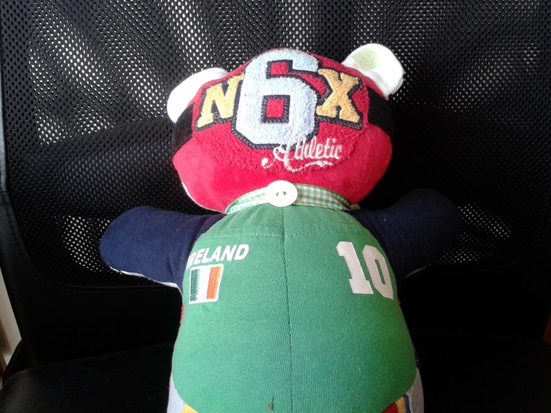 Op de afbeelding: Een pluche teddybeer die een groen-wit shirt draagt met het woord "IRELAND" en het nummer "10" op de rug. De beer draagt ook een rood shirt met de letters "N6X" en het woord "Athletic" op de voorkant.
