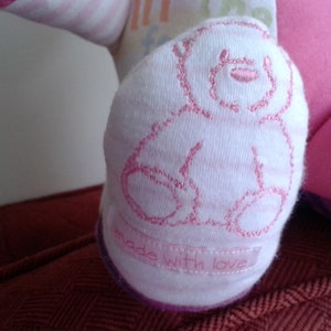 Op de afbeelding: Een witte sok met een roze geborduurd berenontwerp en de tekst "Made with love".
