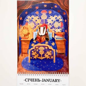 Op de afbeelding: Een wandkalender voor januari met een illustratie van een das die in bed leest, omringd door sterren en distels. De kalender toont de data van de maand, van 1 tot en met 31.