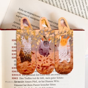 Könnte beinhalten: Satz von vier bunten Lesezeichen mit skurrilen Illustrationen von Kreaturen mit großen Augen und Geweihen. Die Lesezeichen sind in Form von abgerundeten Rechtecken und haben einen braunen Hintergrund mit Herbstblättern. Der Text auf den Lesezeichen lautet "Ein granzend Ziel kann man am ersten trennen. Dies Treffen traf dir fehl, mein guter Schütz: Sie meidet Amors Pfeil, sie hat Dianens Witz. Umsonst hat ihren Panzer keuscher Sitten", und der Hashtag #tukoni.