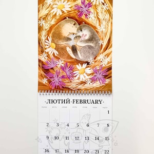Op de afbeelding: Een wandkalender voor februari met een illustratie van een familie otters, omringd door madeliefjes en paarse bloemen. De kalender heeft een spiraalbinding aan de bovenkant. De tekst "ЛЮТИЙ FEBRUARY" is zichtbaar.
