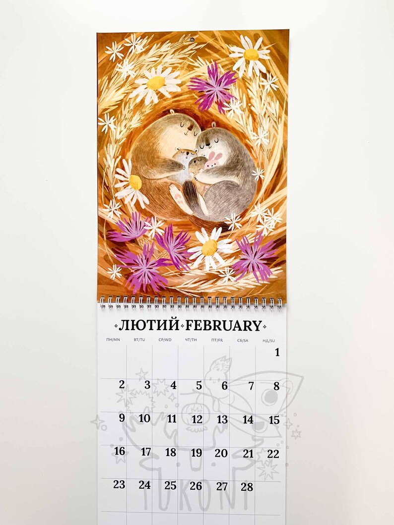 Op de afbeelding: Een wandkalender voor februari met een illustratie van een familie otters, omringd door madeliefjes en paarse bloemen. De kalender heeft een spiraalbinding aan de bovenkant. De tekst "ЛЮТИЙ FEBRUARY" is zichtbaar.