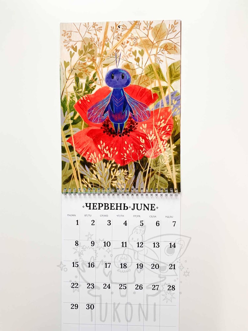 Op de afbeelding: Een kalenderpagina voor juni met een illustratie van een blauw insect met rode en blauwe vleugels op een rode bloem. De kalender toont data en het woord "Juni" in het Engels en Oekra&iuml;ens.