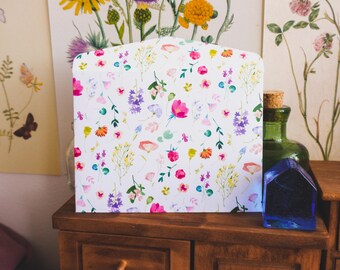 May include: A white envelope with a floral pattern featuring pink, purple, and yellow flowers. The envelope is on a wooden table with a drawer and the text "#tukonitribe" on the front.