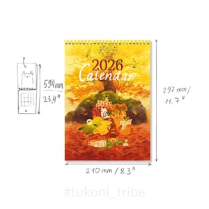 Op de afbeelding: Een 2026-kalender met spiraalbinding, met een herfstthema-illustratie. De kalender is 59,4 cm hoog, 29,7 cm breed en 21 cm diep. De illustratie bevat een bossc&egrave;ne met cartoonfiguren en de tekst "2026 Calendar".