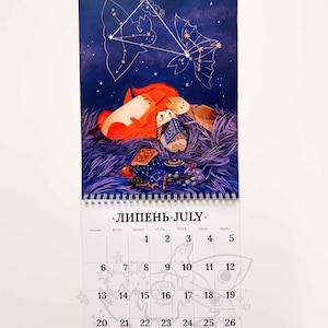 Op de afbeelding: Een juli-kalender met een fantasie-illustratie van een vos, uilen en een theepot onder een sterrenhemel. De kalender heeft een spiraalbinding en een maandelijks overzicht met data en het woord "juli".