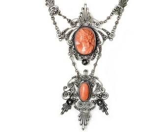 May include: A silver necklace with a delicate filigree design features two oval-shaped cameo pendants with a pink coral color.