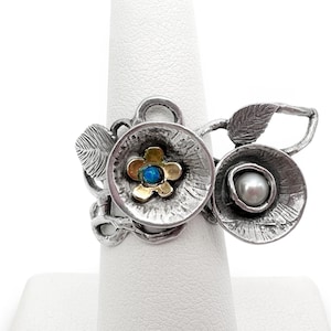 Könnte beinhalten: Ein silberner Ring mit zwei Blumendesigns. Eine Blume hat einen blauen Edelstein in der Mitte und die andere eine Perle.