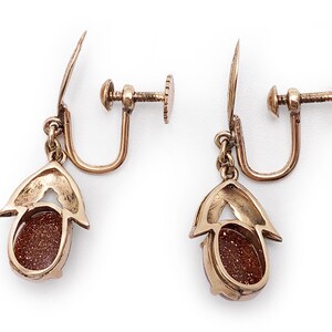 May include: A pair of gold tone clip-on earrings with a brown oval stone set in a gold tone setting.
