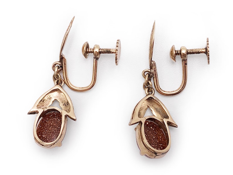 May include: A pair of gold tone clip-on earrings with a brown oval stone set in a gold tone setting.