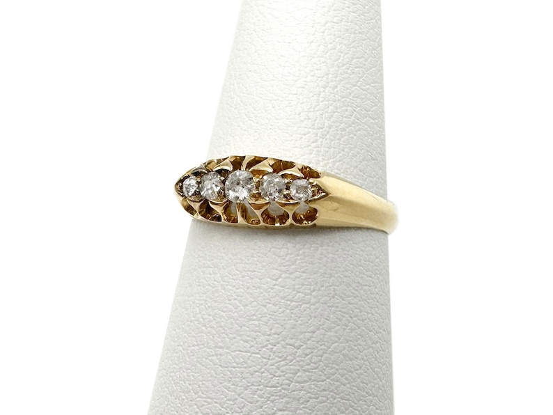 May include: A gold band ring with five clear round diamonds set in a delicate filigree design.