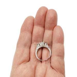 May include: A silver ring with three round stones set in a prong setting. The ring is surrounded by smaller stones.