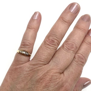 May include: A gold band ring with a row of clear gemstones set in a prong setting.