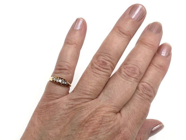 May include: A gold band ring with a row of clear gemstones set in a prong setting.