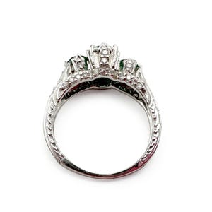 May include: A silver ring with three emerald green stones and a decorative filigree design.
